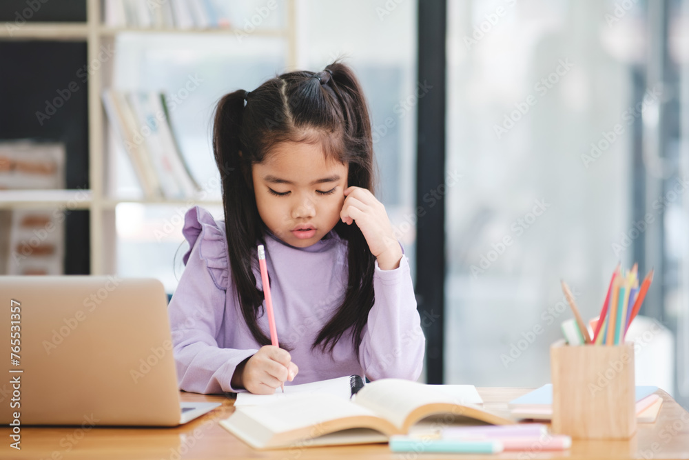 A young girl is sitting at a desk with a laptop and a book A young girl is sitting at a desk with a laptop and a book