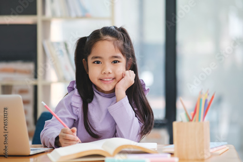 A young girl is sitting at a desk with a laptop and a book © ijeab