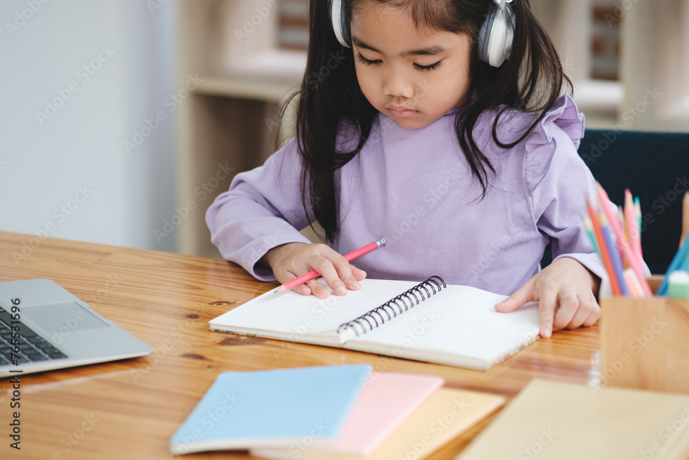 A young girl is sitting at a desk with a notebook and a laptop A young girl is sitting at a desk with a notebook and a laptop