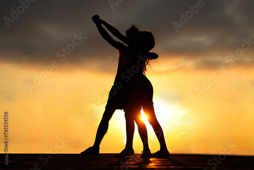 latin hispanic couple is dancing bachata above sea on summer beach. Sunset over water.Two silhouettes against the sun. Just married couple hugging. Romantic love story. Man and woman in holiday trip