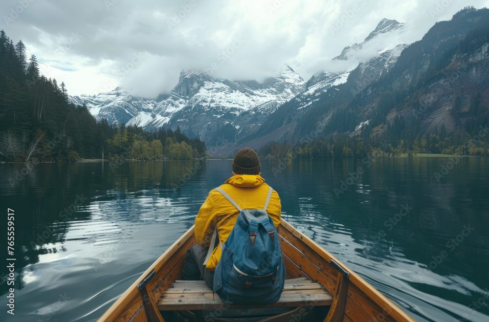 A person sitting in the front of an old wooden boat on Lake passes through mountain lakes, forests and snowy mountains