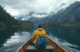 A person sitting in the front of an old wooden boat on Lake passes through mountain lakes, forests and snowy mountains