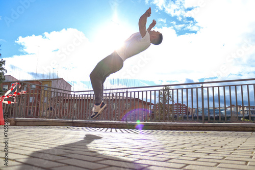 Caucasian man doing a backflip on a pointview with sunlight and sky in background. Urban sport concept photo