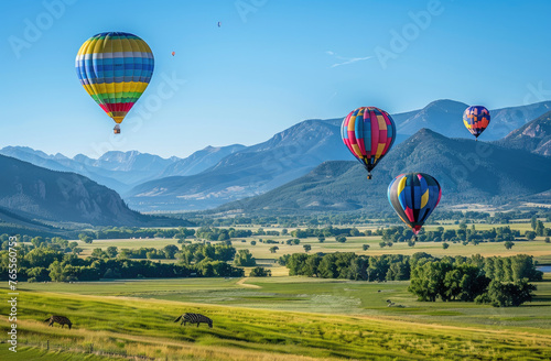 A photo of hot air balloons floating over green fields  with colorful panels on the balloon bodies  against the backdrop of mountains and clear blue skies