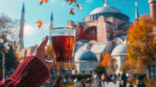 Female hand holding a traditional Turkish glass of tea  against the backdrop of Hagia Sophia