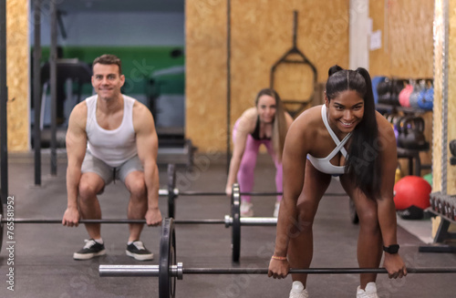 Group of multiracial smiling people doing deadlift with some bars with discs in a gym, front view. Fitness concept