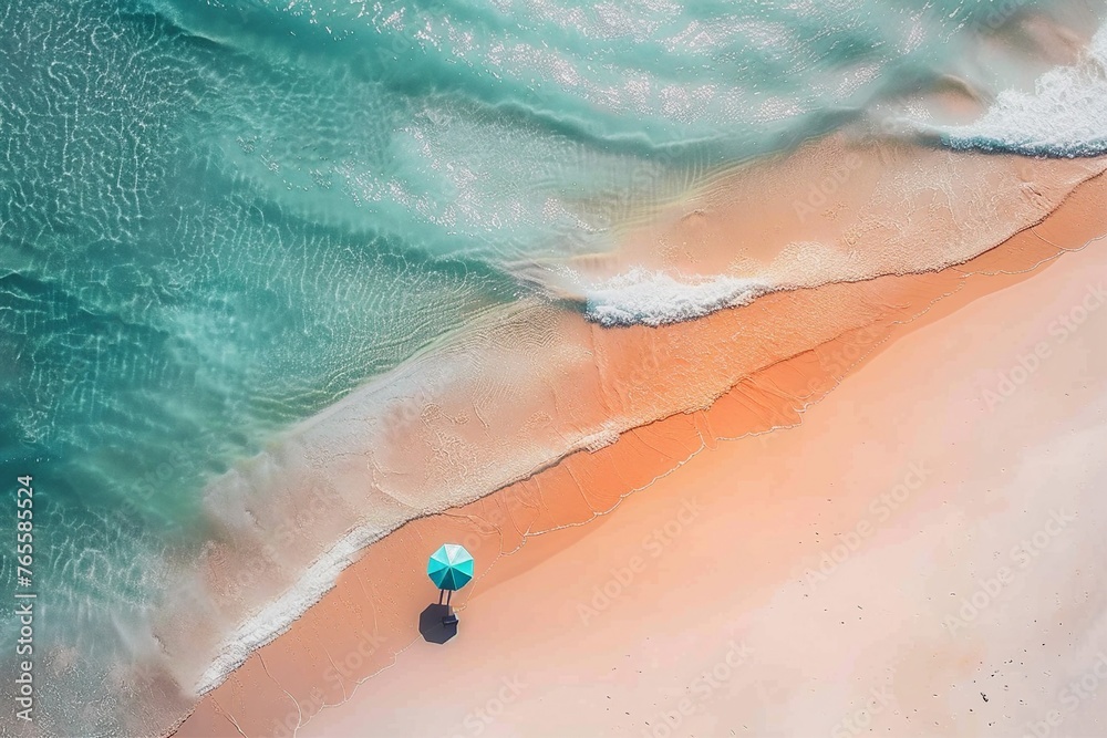 Aerial view of a person standing on a white sandy beach, holding a colorful umbrella with clear blue water and a long exposure effect.