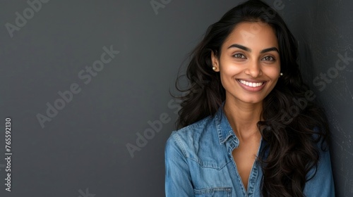 Smiling young Indian business woman wearing blue denim shirt looking at camera isolated on gray empty background.