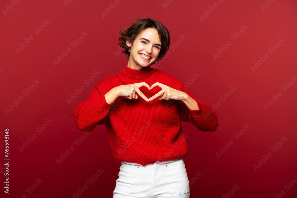 Woman making a heart gesture with her fingers, posing isolated on a red background Woman making a heart gesture with her fingers, posing isolated on a red background