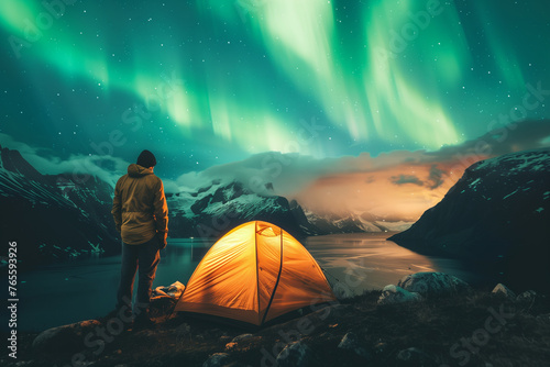 A man camping in wild northern mountains with an illuminated tent viewing a spectacular green northern lights aurora display (1)