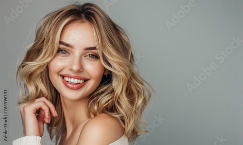 photo of a beautiful blonde woman with shoulder length hair, smiling and posing for the camera against a solid grey background