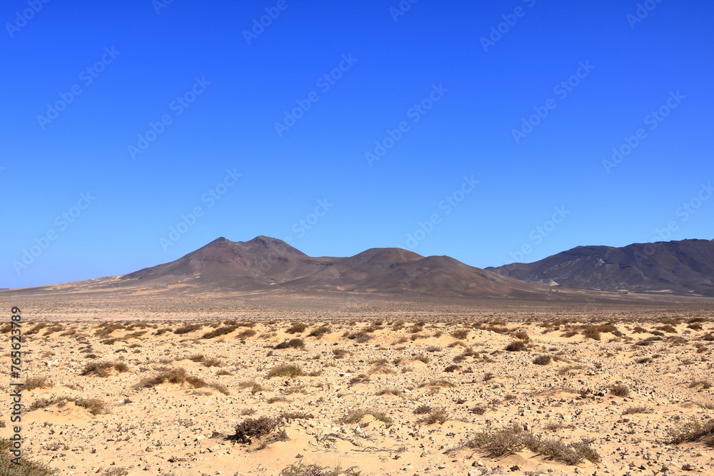 Gravel, dusty road with high volcanic mountains in the background. Jandia, Morro Jable, Fuerteventura, Canary Islands, Spain