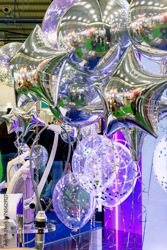 A room with a large number of shiny silver foil balloons, some near the ceiling, others closer to the floor. Balloons emphasize the festive atmosphere.
