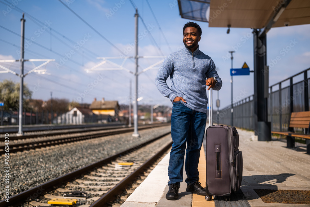 Happy man with suitcase standing on railway station.