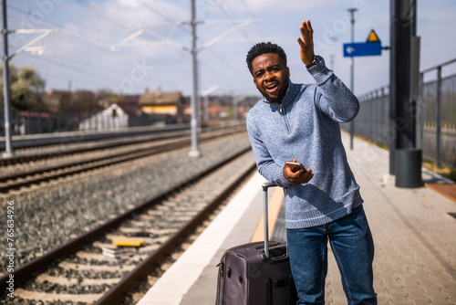 Angry man with a suitcase and mobile phone standing on a railway station.