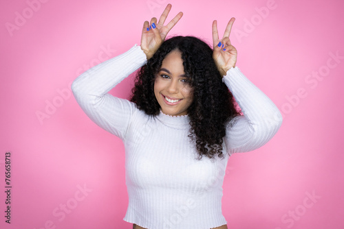 African american woman wearing casual sweater over pink background Posing funny and crazy with fingers on head as bunny ears, smiling cheerful photo