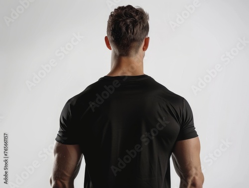 Man stands facing away from camera showing off his back muscles, man stands with his back to the camera in black t-shirt.