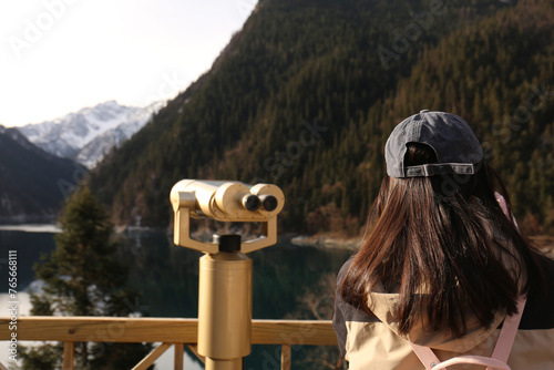 A woman is using binoculars to look at the mountains while she is in the mountains