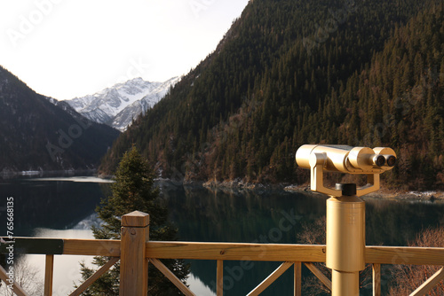 A woman is using binoculars to look at the mountains while she is in the mountains