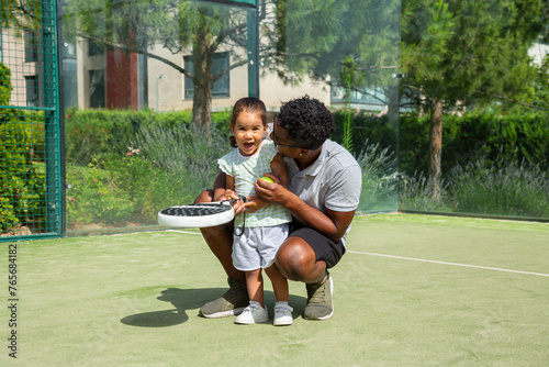 Black father teaching happy daughter to play paddle tennis	