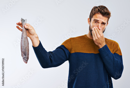 Man, disgust and fish with smelling odor, bad stench of animal or sea creature on a gray studio background. Male person with gross facial expression of disgusted aroma or smelly odd stink on mockup photo