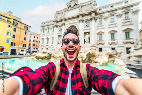 Happy young tourist taking selfie in front of Trevi Fountain during summer vacation in Italy - Happy man enjoying summertime holiday in Europe - Travel and technology life style concept
