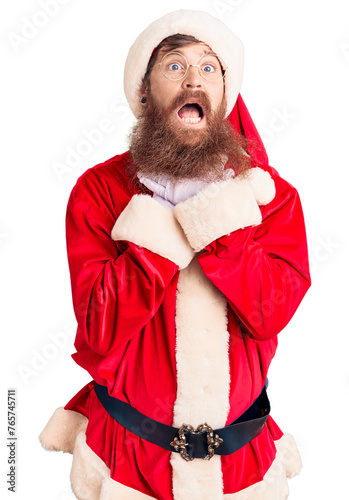 Handsome young red head man with long beard wearing santa claus costume shouting and suffocate because painful strangle. health problem. asphyxiate and suicide concept.
