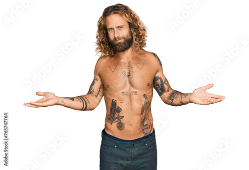 Handsome man with beard and long hair standing shirtless showing tattoos clueless and confused with open arms, no idea concept.