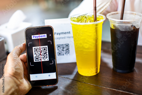 Selective focus to hand using smart phone to scan QR code on tag with blurry chrysanthemum Juice and iced coffee in cafe to accepted generate digital pay without money. Qr code payment concept.