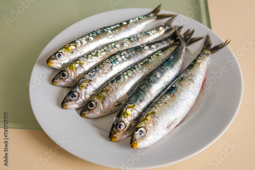 Half a dozen appetizing raw and fresh sardines from the Atlantic Ocean, on a plate. Purchased at the market and from a recently arrived ship. Fishing industry. Healthy and quality foods.