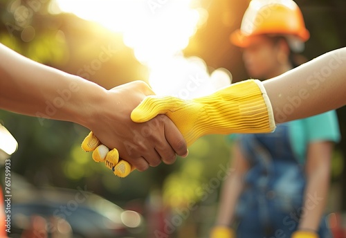Close up of two construction workers shaking hands with other people in the background, sunny day, worker wearing a yellow helmet holding out his hand for a handshake, outdoor setting