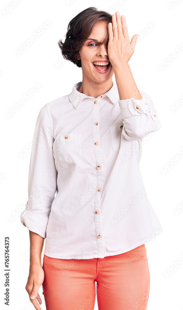 Beautiful young woman with short hair wearing elegant white shirt covering one eye with hand, confident smile on face and surprise emotion. Beautiful young woman with short hair wearing elegant white shirt covering one eye with hand, confident smile on face and surprise emotion.