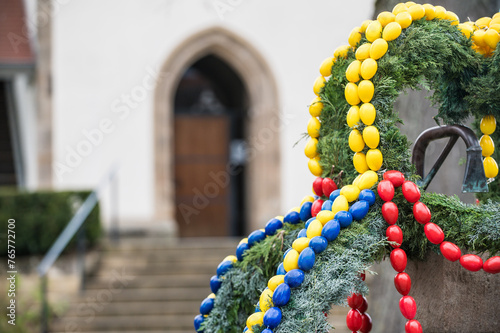 Osterbrunnen mit gelben, roten und blauen Ostereiern aus Kunststoff vor historischem Gebäude photo