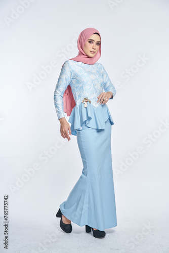Beautiful female model wearing blue peplum dress with hijab, a modern lifestyle outfit for Muslim woman, sitting on a chair isolated over white background. Eidul fitri fashion and beauty concept.