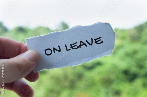 Hand holding torn paper with On Leave text with nature background. Annual leave concept photo