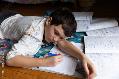 Teenage boy doing homework in his room lying on the floor, he writes in a notebook ,self preparing for school
