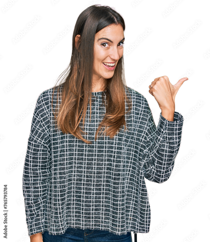 Young beautiful woman wearing casual clothes smiling with happy face looking and pointing to the side with thumb up. Young beautiful woman wearing casual clothes smiling with happy face looking and pointing to the side with thumb up.