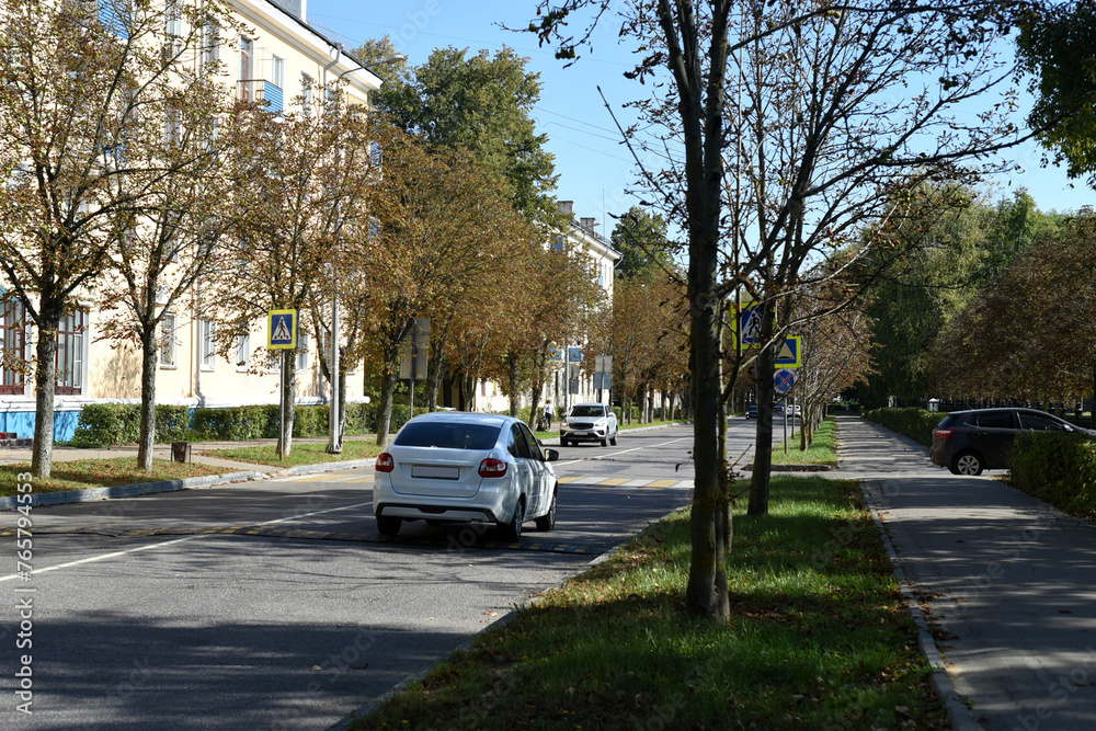 Autumn sunny day on a city street. The sidewalks are deserted, cars are driving along the road.