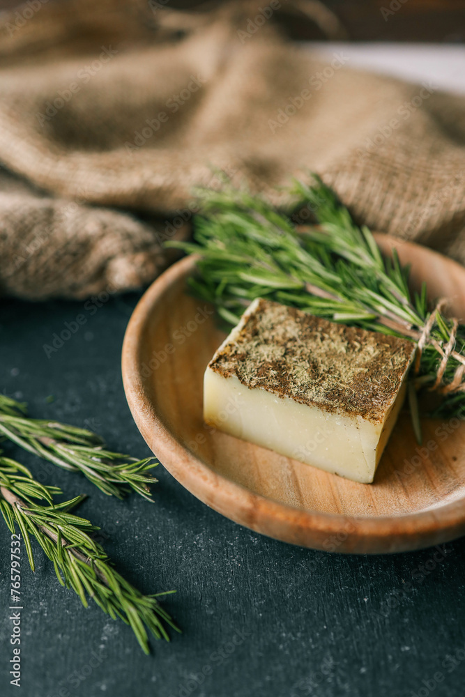 Solid shampoo with rosemary in a wooden plate on a dark background Solid shampoo with rosemary in a wooden plate on a dark background