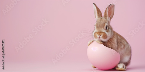 Little Easter bunny hatching from the egg. On a pale pink background. Minimal Easter concept in pastel colors.
