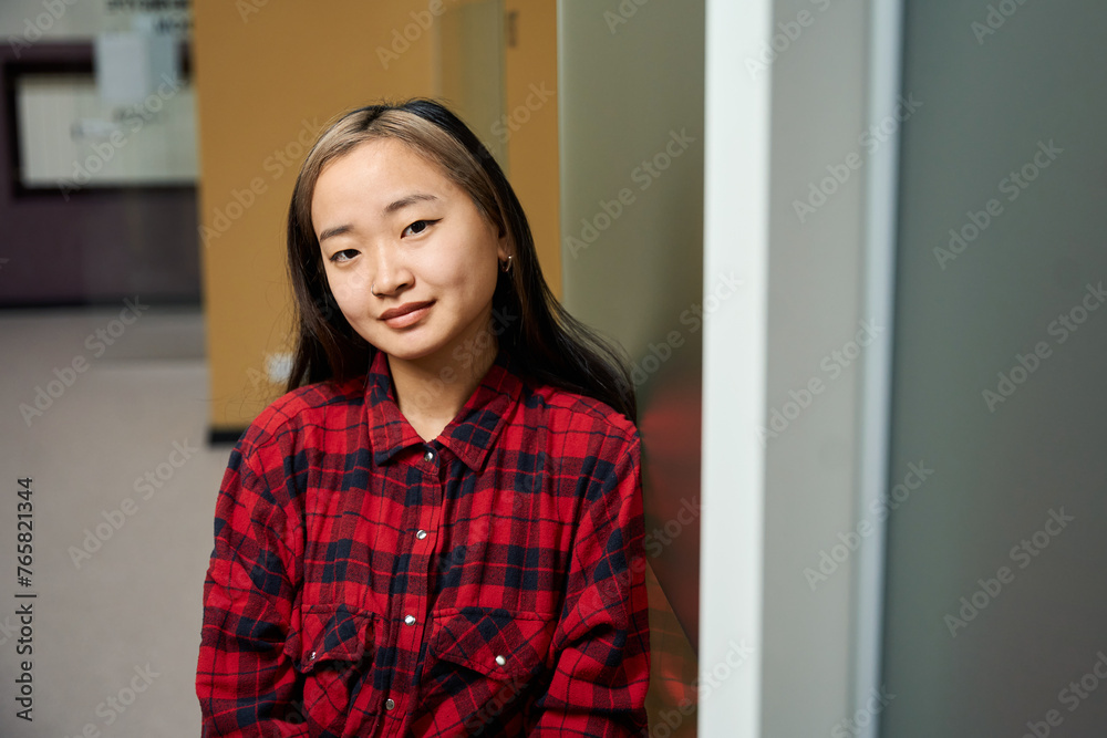 Partial young serious asian female IT worker looking at camera by wall in office Partial young serious asian female IT worker looking at camera by wall in office