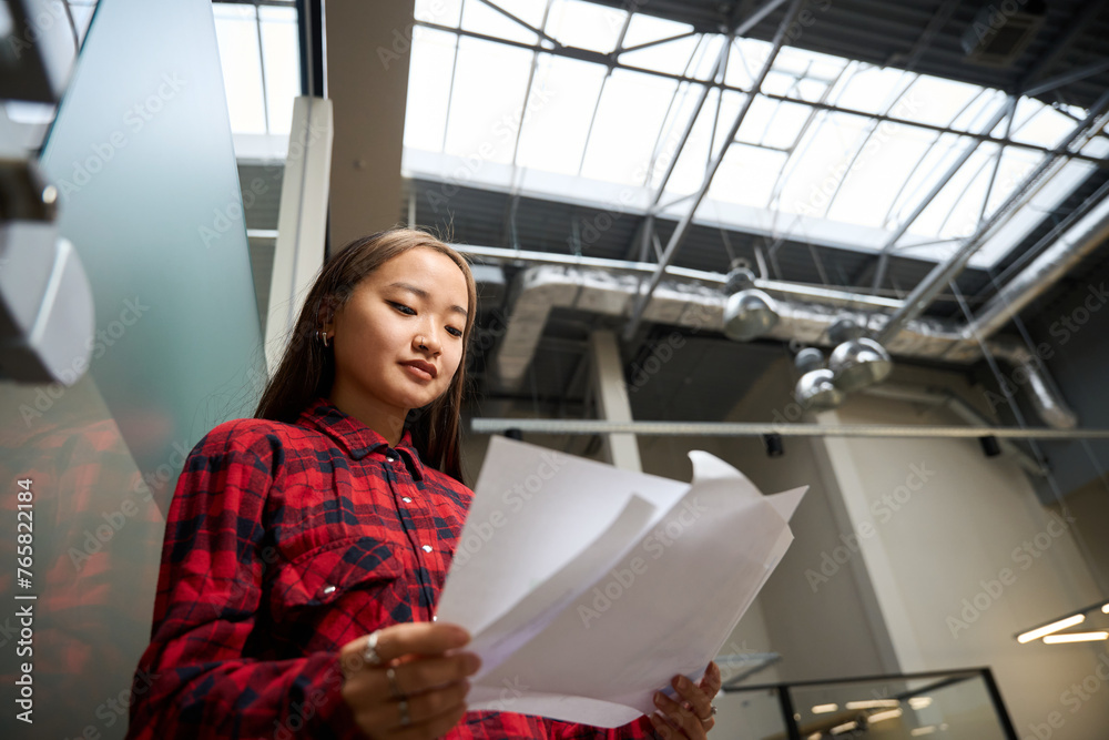 Bottom view of young concentrated asian female IT employee reading documents Bottom view of young concentrated asian female IT employee reading documents