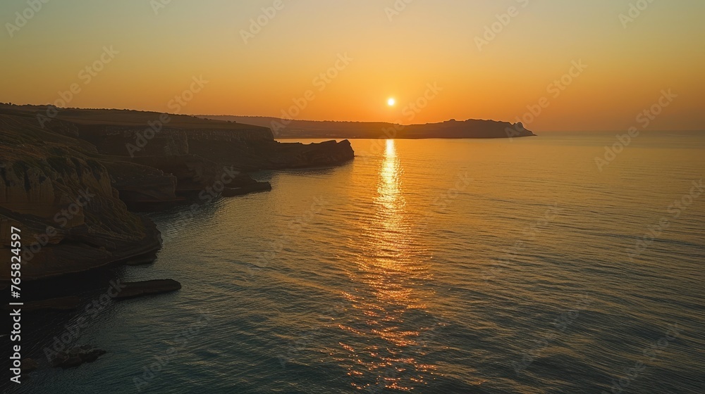 Fototapeta premium A tranquil sunset over a calm sea with cliffs on one side.