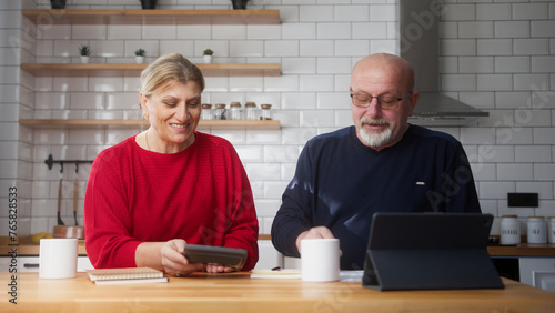 Senior retired couple sit in kitchen doing paperwork, checking calculating bills bank loan payment, discuss unpaid debt taxes. Old grandparents family money problem concept	
 photo