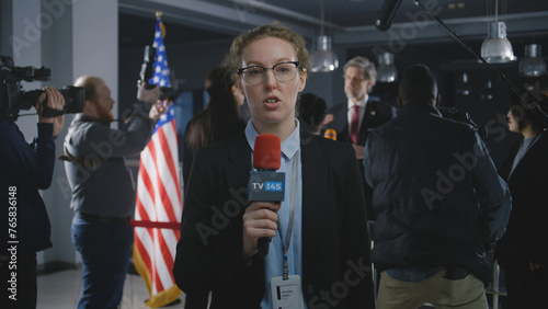 Caucasian anchorwoman reports breaking news live from government building. Female journalist leads broadcast for political TV program from press conference with American politician or US President. photo