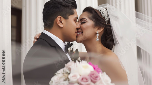 A bride and groom are affectionately touching foreheads, smiling on their wedding day.