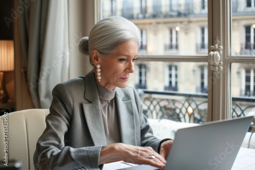 Attractive mature businesswoman working on laptop computer while sitting in office in paris. 