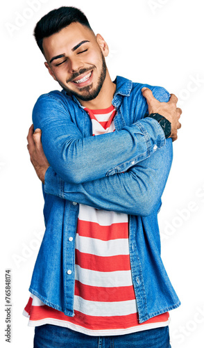 Young hispanic man with beard wearing casual denim jacket hugging oneself happy and positive, smiling confident. self love and self care