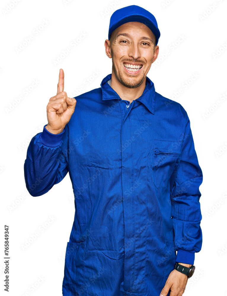 Bald man with beard wearing builder jumpsuit uniform showing and pointing up with finger number one while smiling confident and happy.