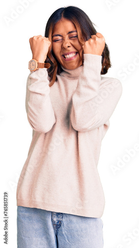 Young beautiful mixed race woman wearing winter turtleneck sweater excited for success with arms raised and eyes closed celebrating victory smiling. winner concept.